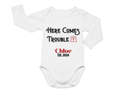 a white bodysuit with the words here comes trouble on it