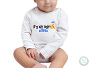 a baby sitting on the ground wearing a white bodysuit